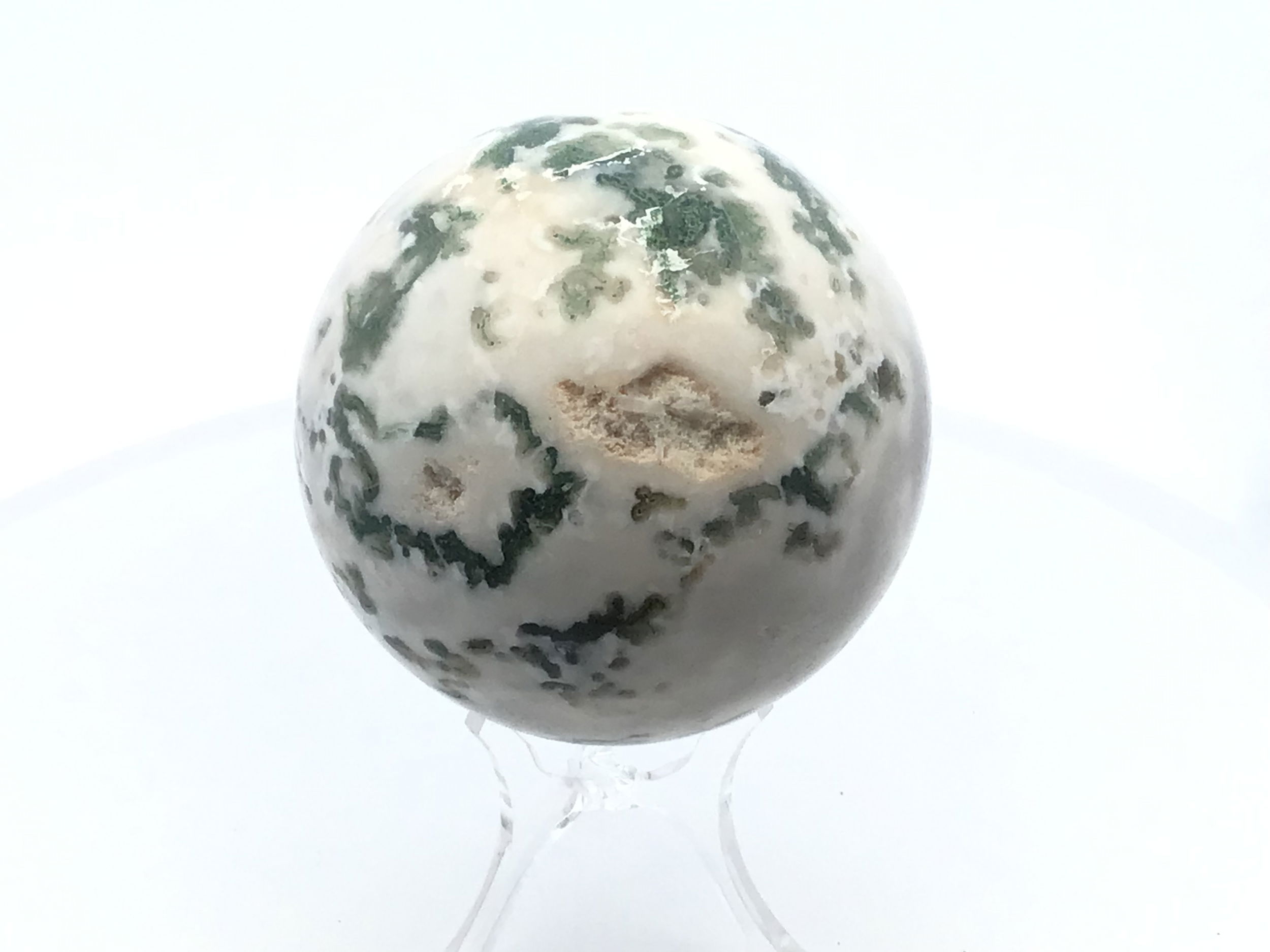 Polished to a smooth, radiant sphere, this genuine Moss Agate captures enchanting forest-green inclusions and earthy patterns, each piece uniquely reflecting nature’s artistry. Resting on a minimalist Lucite stand, it offers a modern display that complements any setting—from meditation spaces to office desks.Cherished for its grounding and nurturing qualities, Moss Agate inspires balance, renewal, and a deeper connection to the natural world. This sphere is an elegant addition to crystal collections or a meaningful gift for those drawn to earth’s tranquil energy. Moss Agate Sphere with Lucite Stand