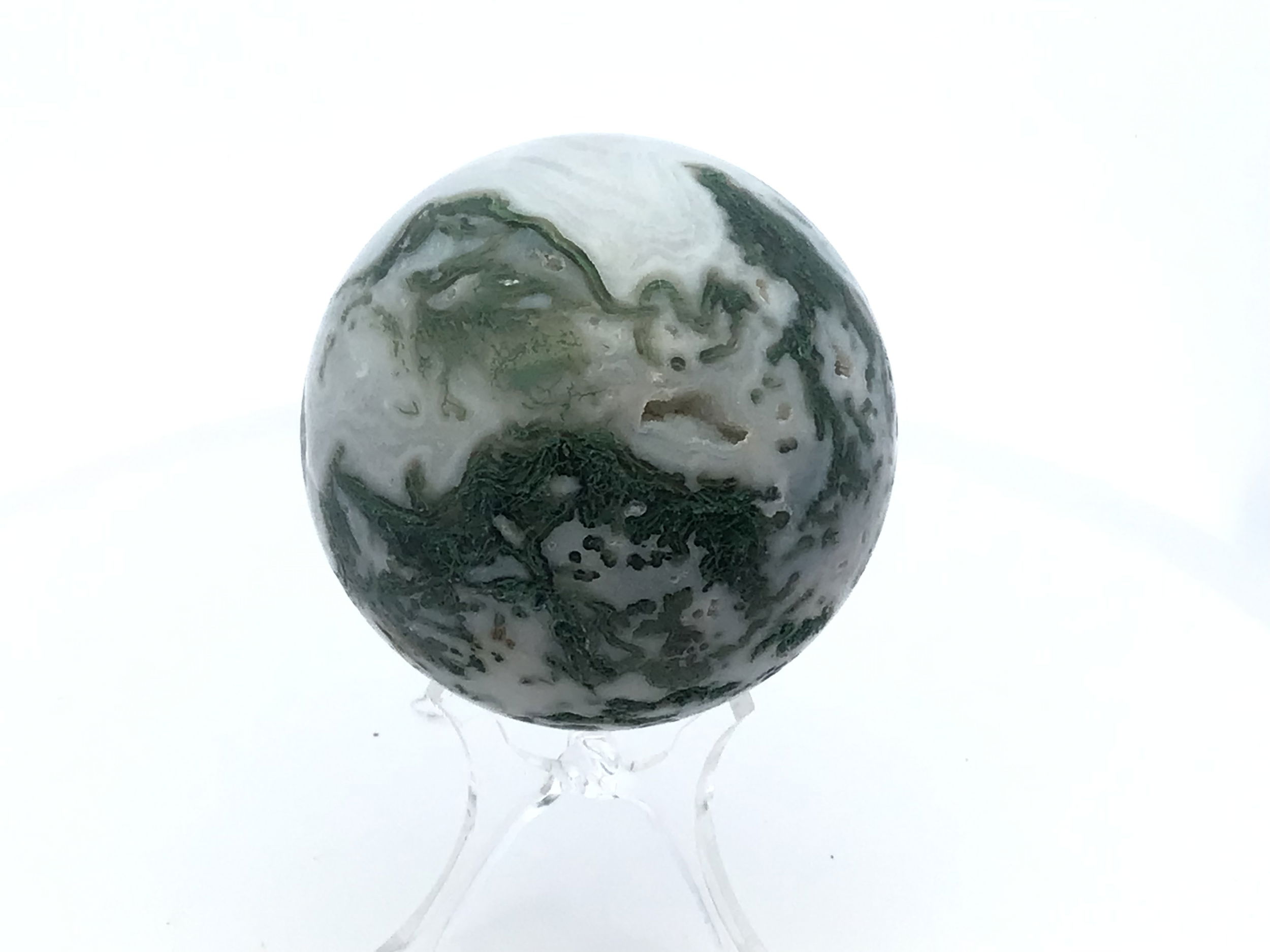 Polished to a smooth, radiant sphere, this genuine Moss Agate captures enchanting forest-green inclusions and earthy patterns, each piece uniquely reflecting nature’s artistry. Resting on a minimalist Lucite stand, it offers a modern display that complements any setting—from meditation spaces to office desks.Cherished for its grounding and nurturing qualities, Moss Agate inspires balance, renewal, and a deeper connection to the natural world. This sphere is an elegant addition to crystal collections or a meaningful gift for those drawn to earth’s tranquil energy. Moss Agate Sphere with Lucite Stand