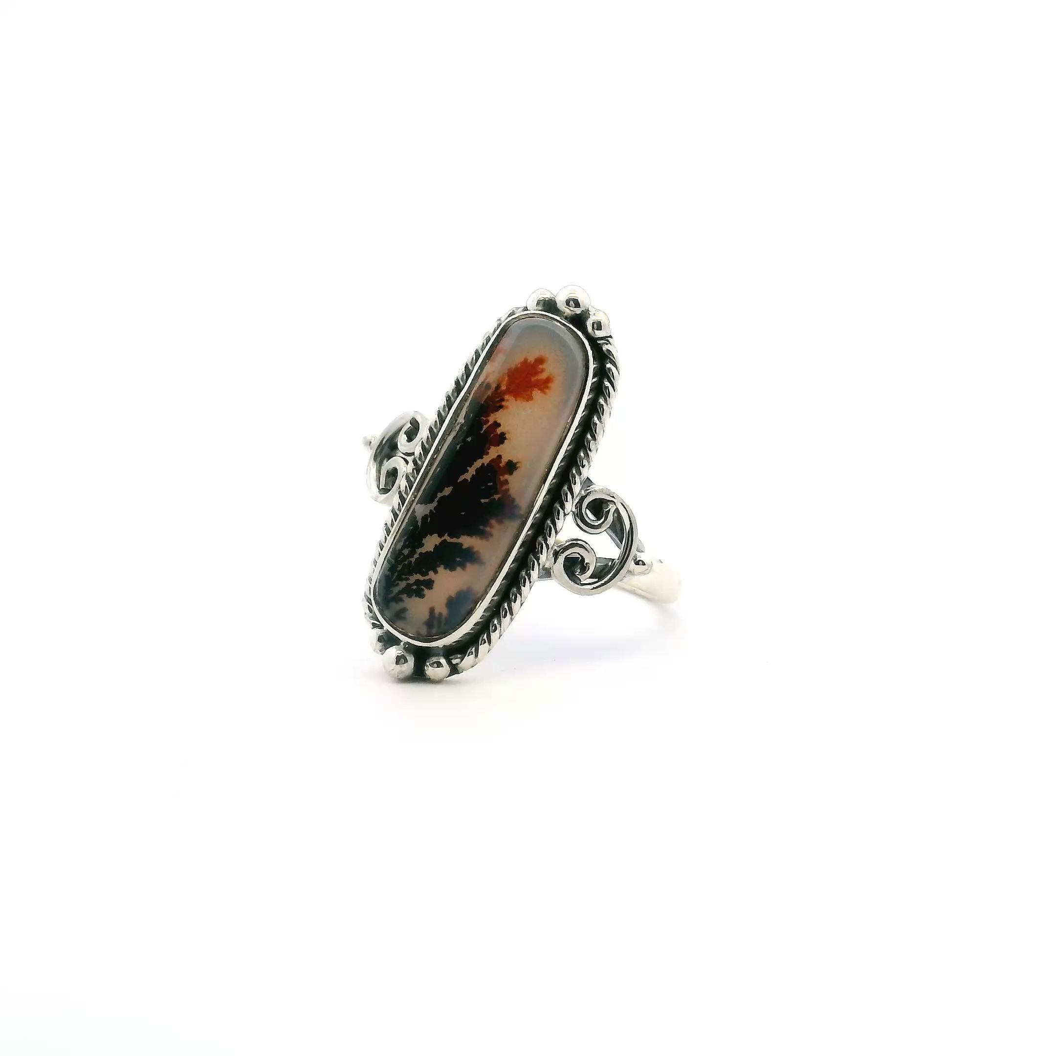 Discover natural elegance with this Dendritic Agate Ring, featuring a unique rounded rectangle cabochon adorned with vivid orange and deep brown dendritic inclusions that evoke tranquil landscapes. The gemstone is bezel-set in lustrous 925 sterling silver, highlighted by intricate rope and beaded detailing that adds artisanal charm. Sized perfectly at 7, this handcrafted ring infuses any look with earthy sophistication—ideal for daily wear or special occasions. Dendritic Agate Ring - Rounded Rectangle Cabochon with Orange & Dark Brown Dendrites & Rope & Beaded Detail Bezel Set in 925 Sterling Silver sz7