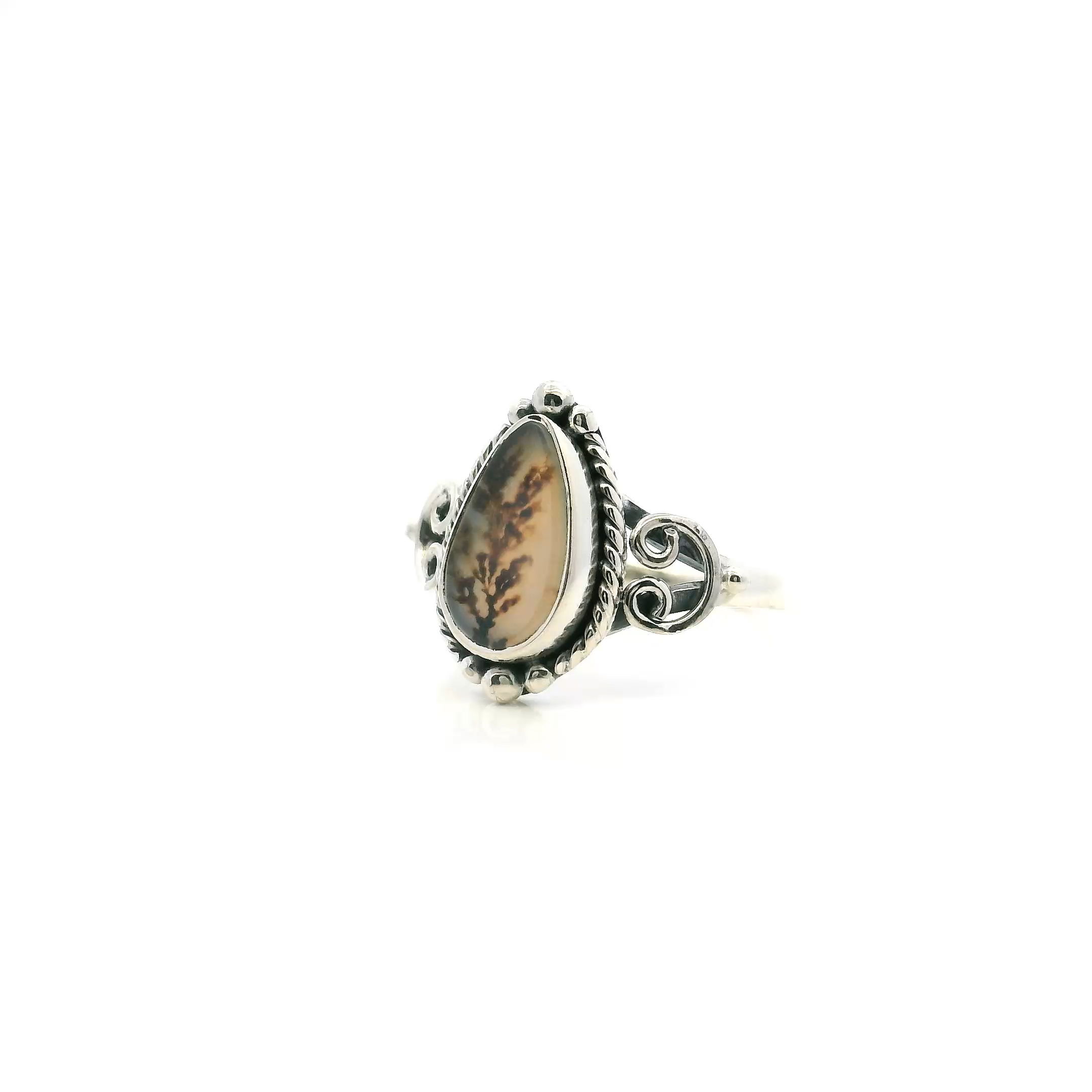 Discover the enchanting beauty of our Dendritic Agate Ring, featuring a striking pear cabochon adorned with intricate dark brown dendrites. Expertly bezel-set in luminous 925 sterling silver, this ring boasts exquisite rope and beaded detailing around the setting, adding a touch of artisanal charm. Perfectly sized at 7, this elegant piece is a natural statement for any jewelry lover. Elevate your collection with this unique women's ring—where timeless style meets earthy sophistication. Dendritic Agate Ring - Pear Cabochon with Dark Brown Dendrites & Rope & Beaded Detail Bezel Set in 925 Sterling Silver sz7