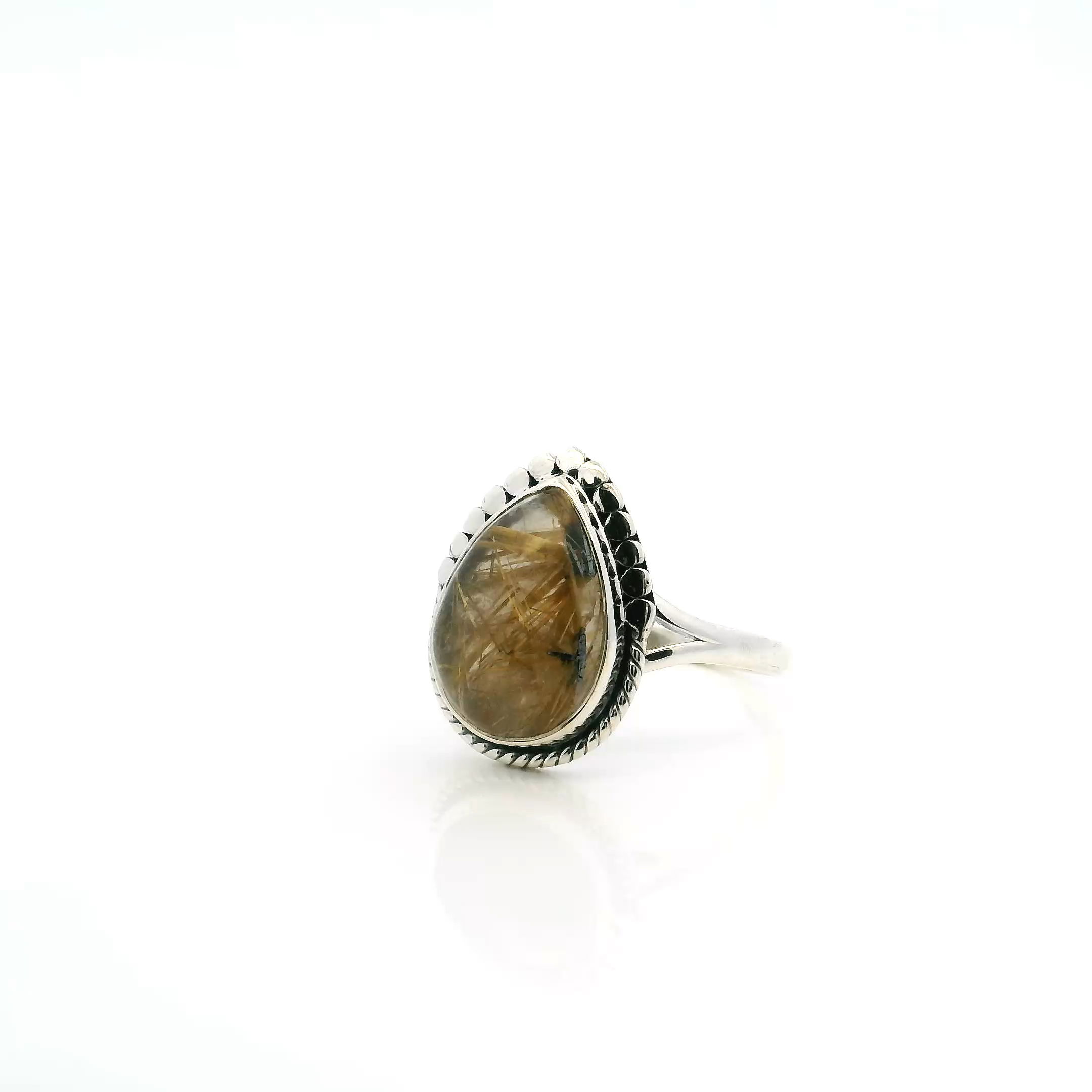 Make a bold yet elegant impression with this Golden Rutilated Quartz Ring, showcasing a luminous pear-shaped cabochon threaded with vivid golden rutile in rare Z-shaped formations. Framed in detailed rope and beadwork and securely bezel set in solid 925 sterling silver, the stone’s natural brilliance takes center stage. The double band design adds a refined touch and ensures a comfortable, balanced fit in size 8. A stunning blend of texture, sparkle, and timeless craftsmanship, this ring is perfect for anyone drawn to the uncommon beauty of nature captured in fine, handcrafted jewelry. Golden Rutilated Quartz Ring - Pear Cabochon with Z-Shape Gold Rutile Bezel Set with Rope & Flattened Bead Detail on Double Band in 925 Sterling Silver sz8