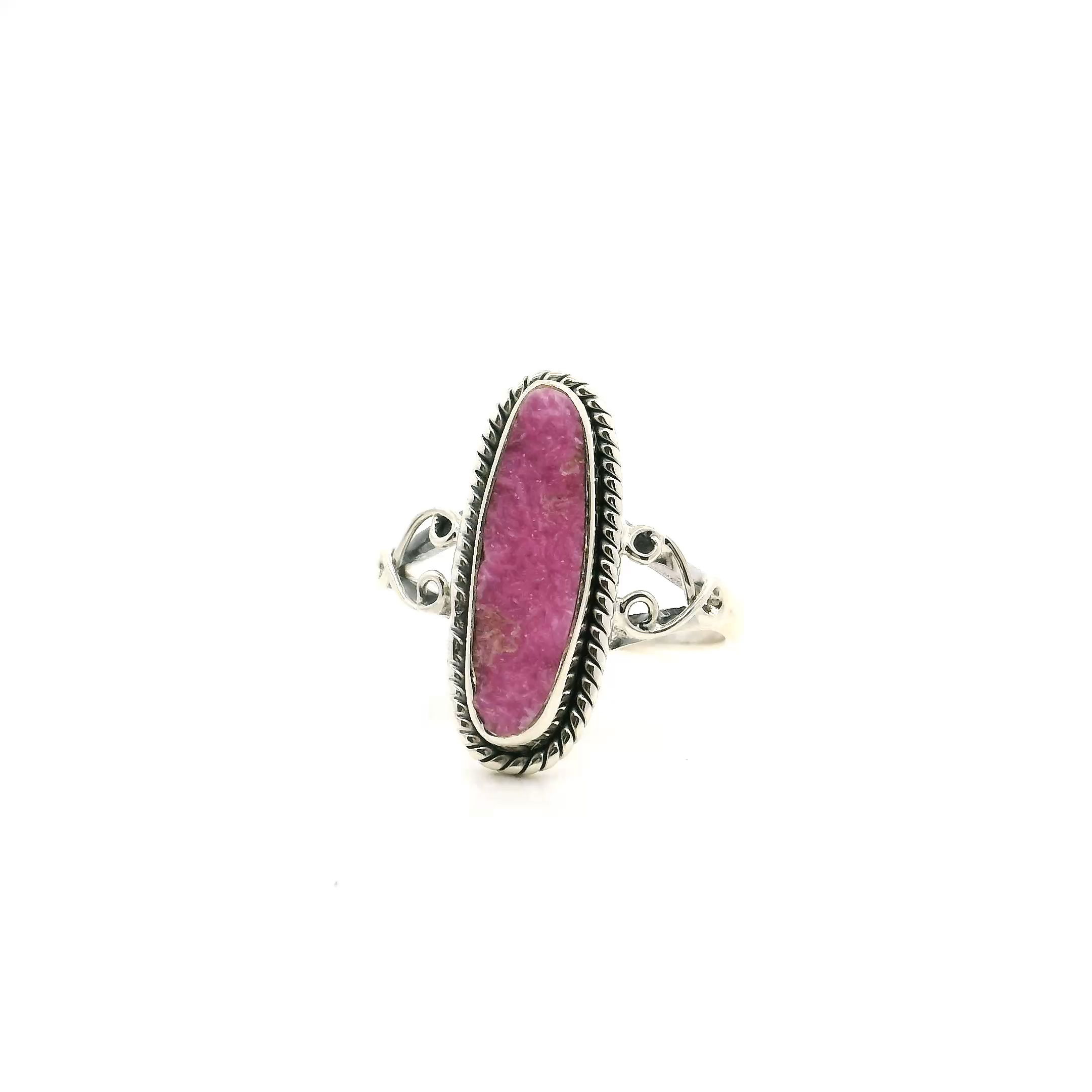 Elevate your style with this captivating Cobalt Calcite Ring, expertly crafted in a size 7 for the modern woman. Featuring an elongated oval cabochon of vibrant pink cobalt calcite, the centerpiece boasts enchanting druzy textures that shimmer with every movement. The stone is bezel-set in lustrous 925 sterling silver, accentuated by intricate rope detail encircling the gem for a touch of vintage charm. Thoughtful wishbone side accents add a subtle, symbolic flourish to the silhouette. Sophisticated and unique, this ring is a stunning addition to any jewelry collection—perfect for those who seek elegance with a bold, artisan-crafted twist. Cobalt Calcite Ring - Elongated Oval with Pink Druzy & Rope Detail & Wishbone Side Accents Bezel Set in 925 Sterling Silver sz7