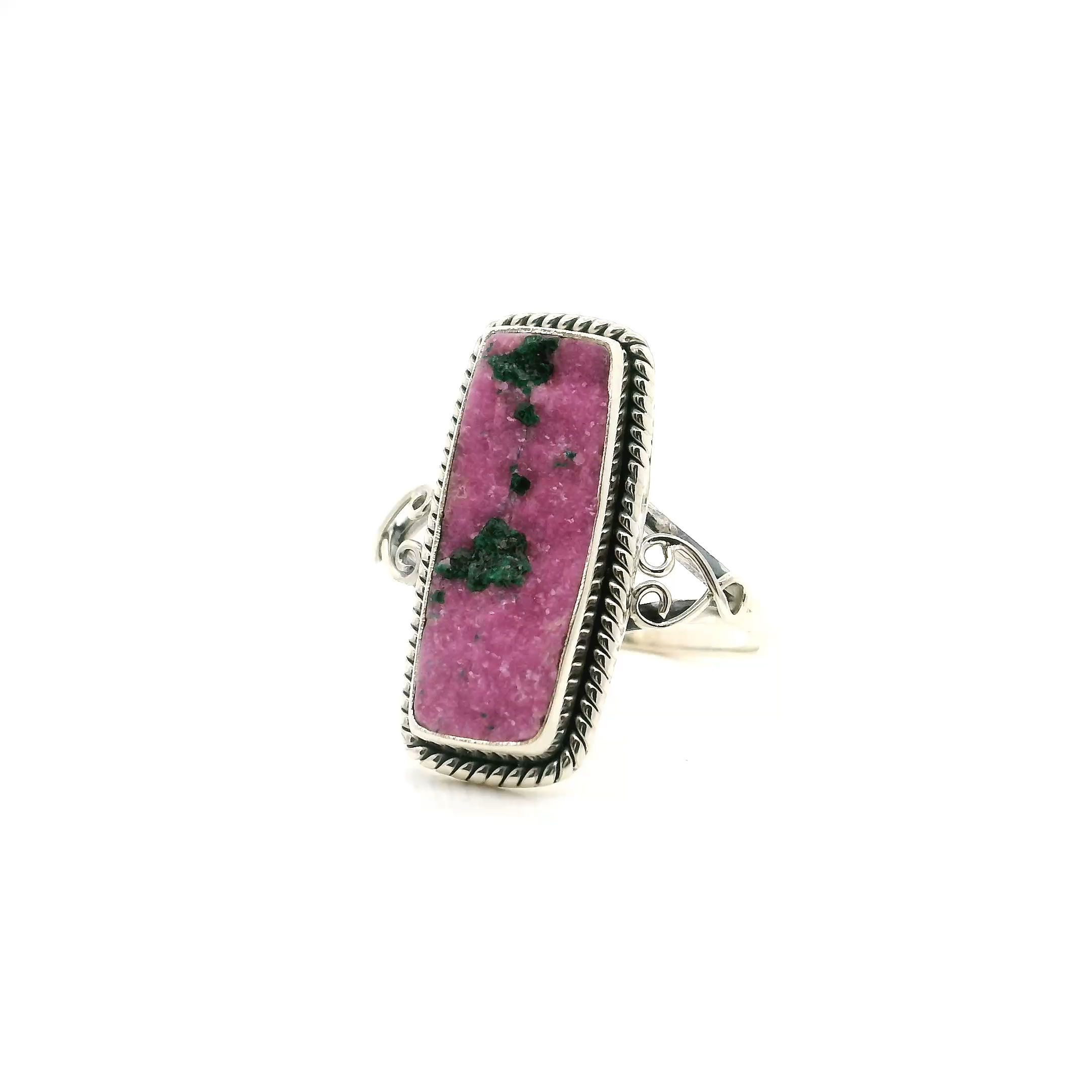 Make a statement with this unique Cobalt Calcite Ring, crafted in luminous 925 sterling silver. Showcasing an elongated rectangle of vivid pink cobalt calcite, this one-of-a-kind piece dazzles with natural druzy sparkle, and features striking fibrous malachite inclusions for a captivating pop of green. Intricate rope detailing frames the bezel set stone, while gracefully sculpted wishbone accents adorn the sides, infusing the ring with an elegant touch. Perfectly sized for comfort at size 9, this artisanal ring is a dazzling addition to any jewelry collection and a stunning choice for those who seek rare and enchanting gemstones. Cobalt Calcite Ring - Elongated Rectangle with Pink Druzy & Fibrous Malachite Inclusions with Rope Detail & Wishbone Side Accents Bezel Set in 925 Sterling Silver sz9