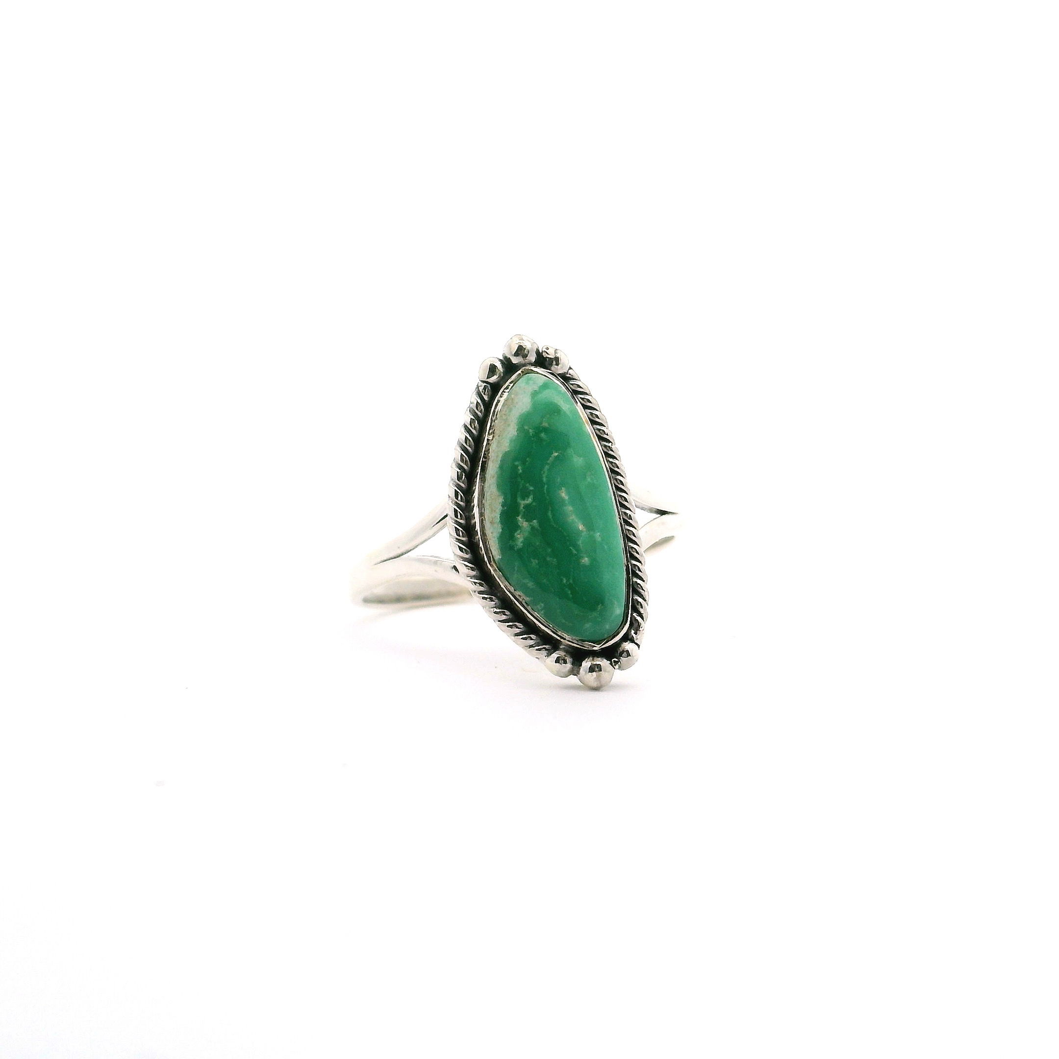 Discover the captivating allure of our Variscite Ring, featuring a striking elongated freeform cabochon glowing with rich green hues reminiscent of tranquil coastal landscapes. Set in a dark green beach bezel, the centerpiece is accentuated by intricate rope and beaded detailing that adds a touch of bohemian elegance. Crafted in 925 sterling silver, the double band design ensures both durability and distinctive style, perfect for daily wear or special occasions. This size 8 ring is a unique addition to any jewelry collection, blending natural beauty and artisan craftsmanship for a statement piece you'll treasure. Variscite Ring - Elongated Freeform Cabochon with Dark Green Beach Bezel Set with Rope & Beaded Detail on Double Band in 925 Sterling Silver sz8