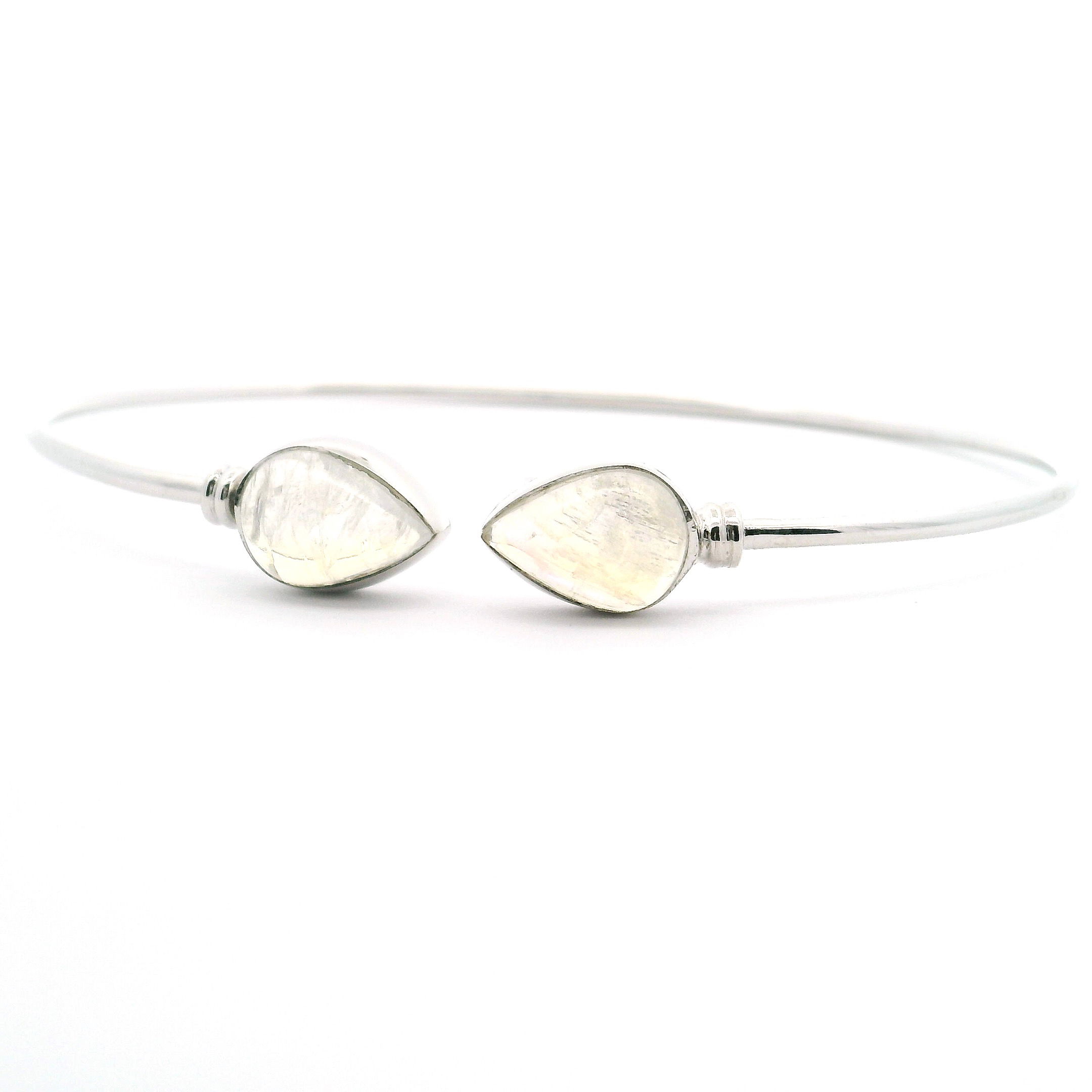 Illuminate your wrist with ethereal elegance wearing the Rainbow Moonstone Twist Bracelet. This captivating cuff is expertly crafted from 925 sterling silver and features two stunning pear-shaped cabochon rainbow moonstones, each bezel-set as luminous centerpiece accents. Delicate side details enhance the open twist design, creating a graceful interplay of shimmering light and contemporary form. Rainbow Moonstone Twist Bracelet - Double Pear Cabochon Bezel Set with Side Accents on Open Twist Cuff in 925 Sterling Silver