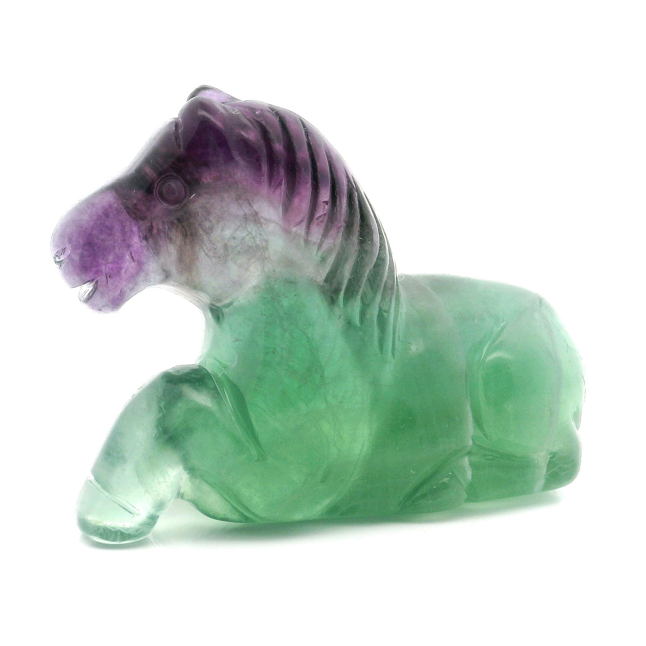Elevate your space with the captivating beauty of this Green and Purple Fluorite Horse Carving. Expertly sculpted in a serene laying down posture, this unique piece highlights the natural banding and vibrant hues of genuine fluorite, blending calming greens with royal purples. Each horse is meticulously hand-carved, making it a one-of-a-kind collectible—perfect for crystal lovers, equestrian enthusiasts, or anyone seeking a harmonious and elegant accent for their home or office. Ideal as a thoughtful gift or a meaningful addition to your own collection, this fluorite horse is a striking embodiment of strength, grace, and tranquility. Green and Purple Fluorite Horse Carving - Laying Down Posture