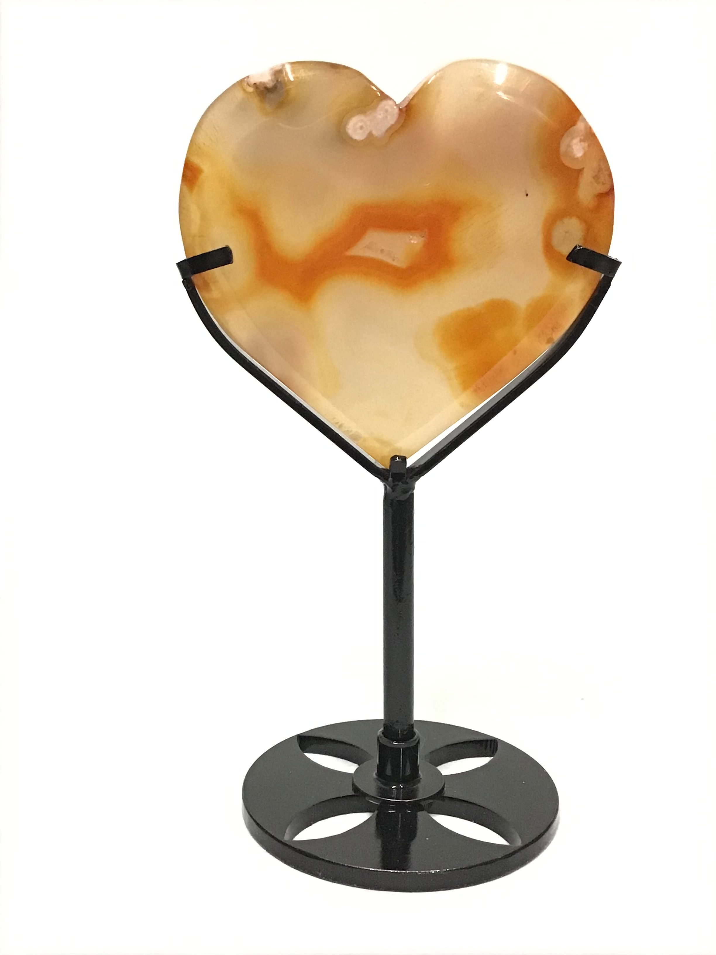 Illuminate your space with the radiant energy of our Flower Carnelian Heart, elegantly displayed on a fitted metal stand. This captivating piece features a striking blend of light translucent yellow hues, accentuated by vivid orange banding and intriguing black inclusions. Meticulously carved into a heart-shaped geometric form, each crystal showcases the natural beauty and unique patterns of genuine Carnelian, renowned for its vitality and warmth. Flower Carnelian Heart on Fitted Metal Stand - Light Translucent Yellow with Bright Orange Banding & Black Inclusions