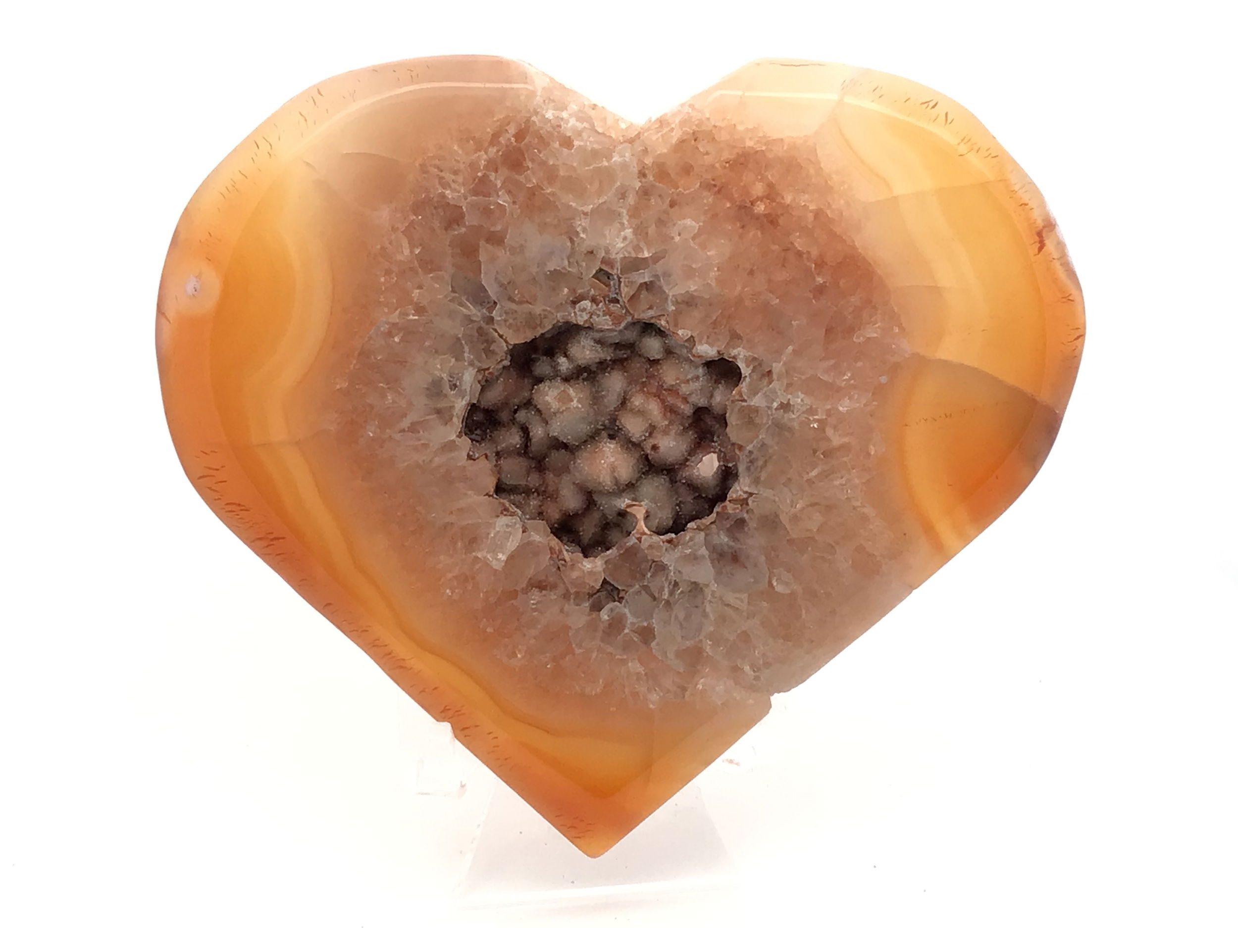 Elevate your space with this stunning Sardonyx Carnelian Agate Heart Flat, artfully displayed on a sleek Lucite stand. Featuring glowing light yellow edges swirling around a central peachy quartz band, this piece captivates with its richly layered color play. The highlight is a distinctive peach druzy pocket, sparkling with intricate inclusions that form natural geometric shapes and charming hearts. Each crystal radiates warmth and grounding energy, making this unique mineral specimen a gorgeous addition to any crystal collection or interior decor. Sardonyx Carnelian Agate Heart Flat with Druze on Lucite Stand - Light Yellow Edges Around Peachy Quartz Band with Interesting Peach Druze Pocket with Multiple Inclusions