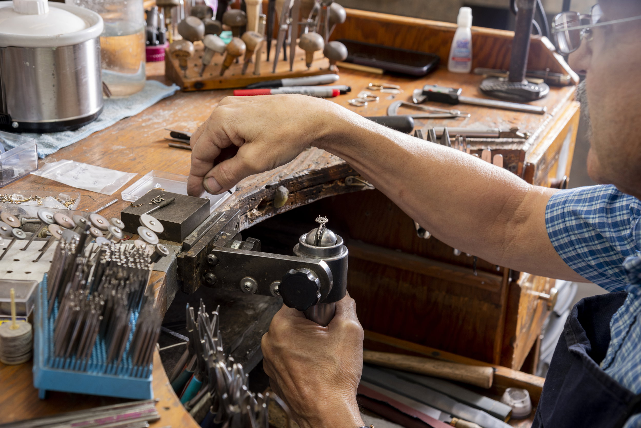 Bench jeweler's hands stringing a pearl necklace at a work table