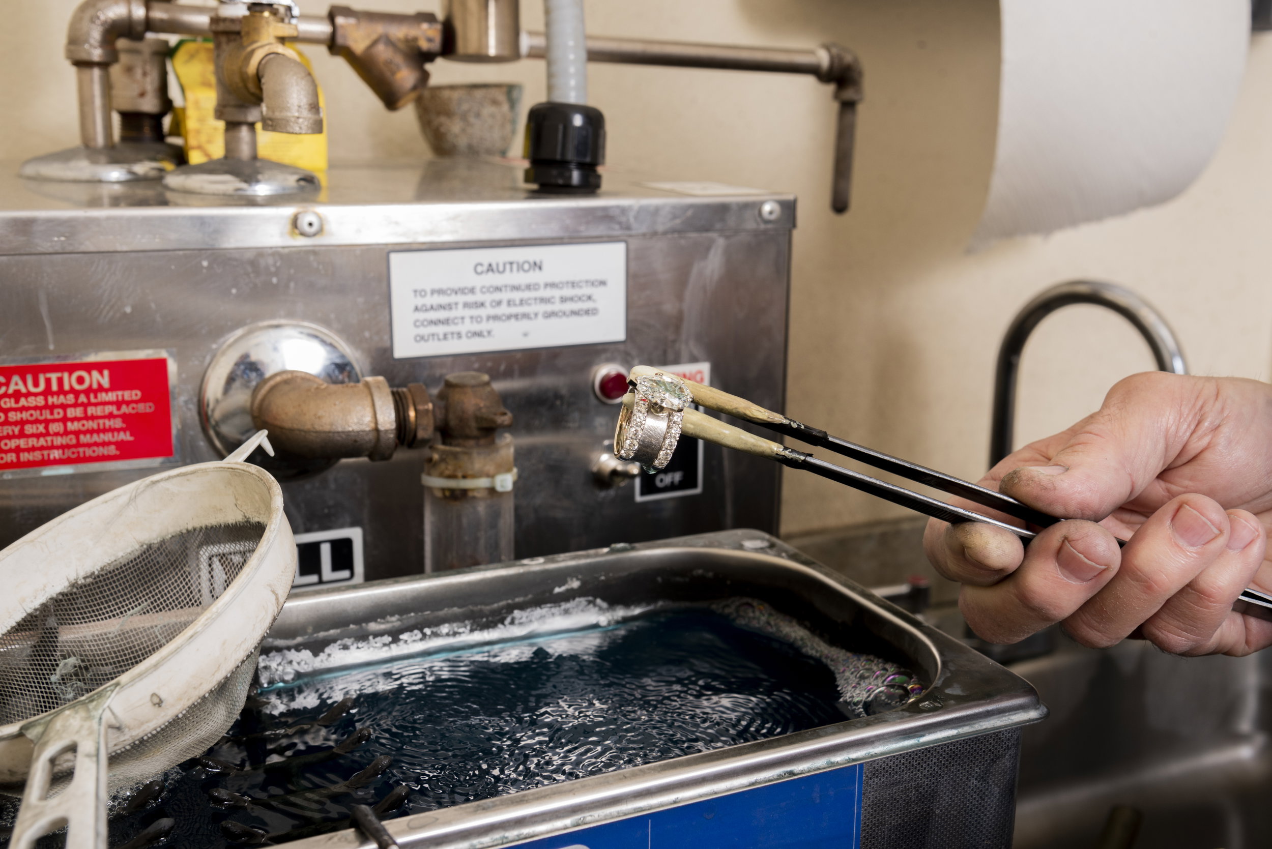 Bench jeweler's hands stringing a pearl necklace at a work table