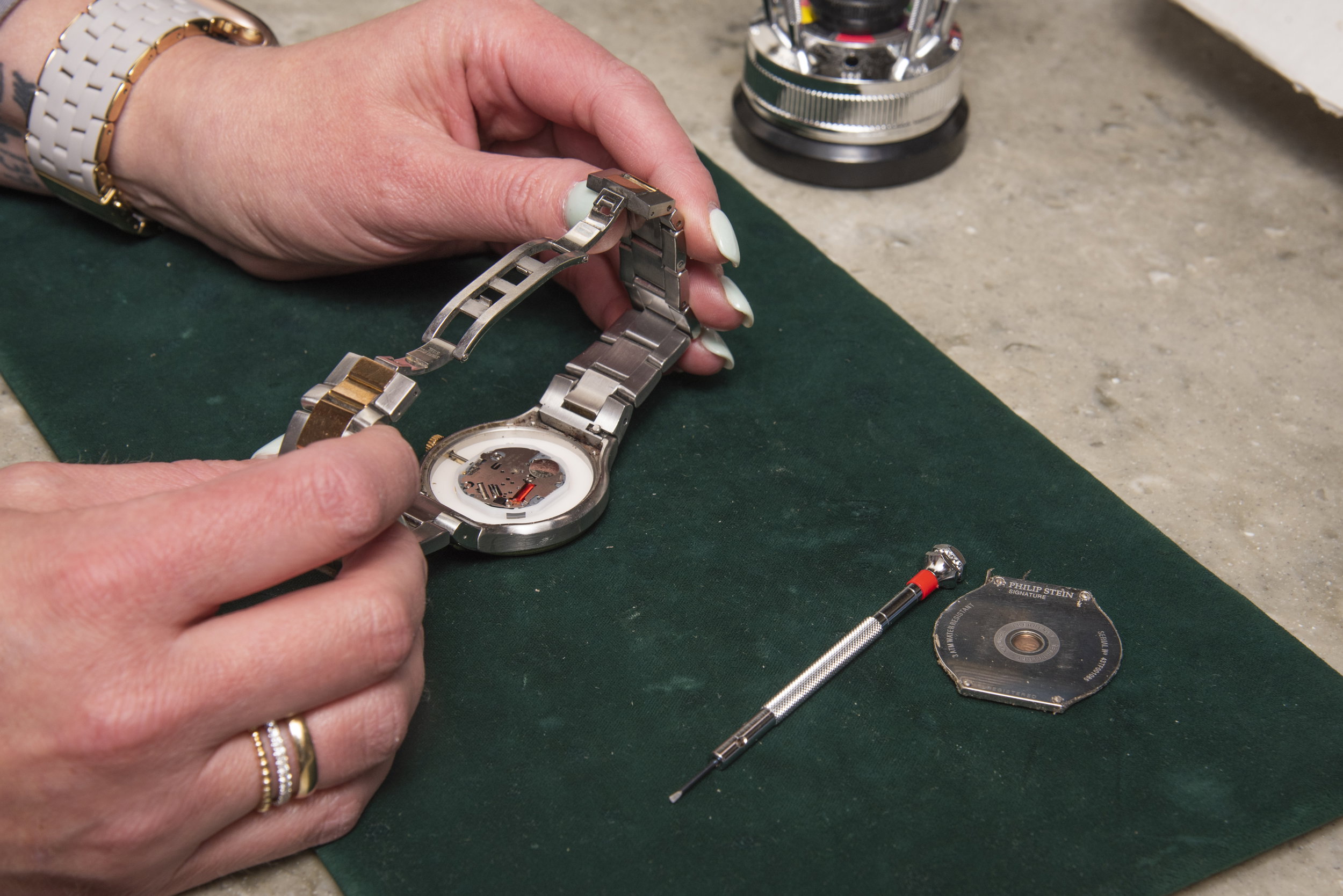 Watchmaker's hands working on the internal movement of a silver watch casing over a green felt mat