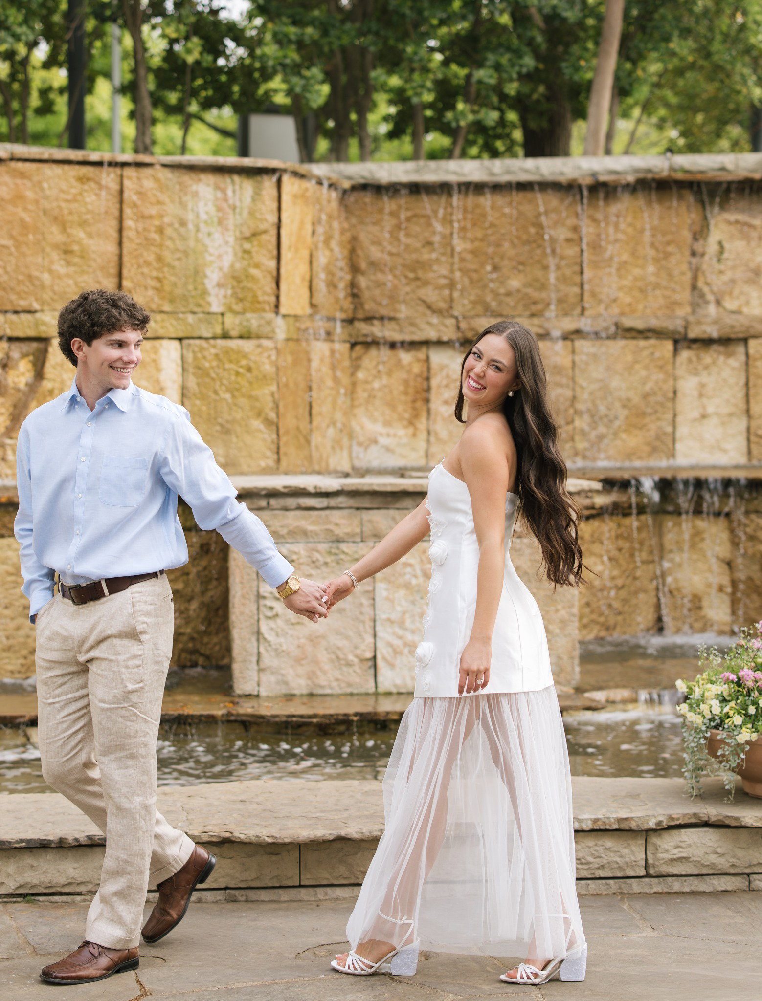 Madi Grace and her fiance holding hands by a fountain.