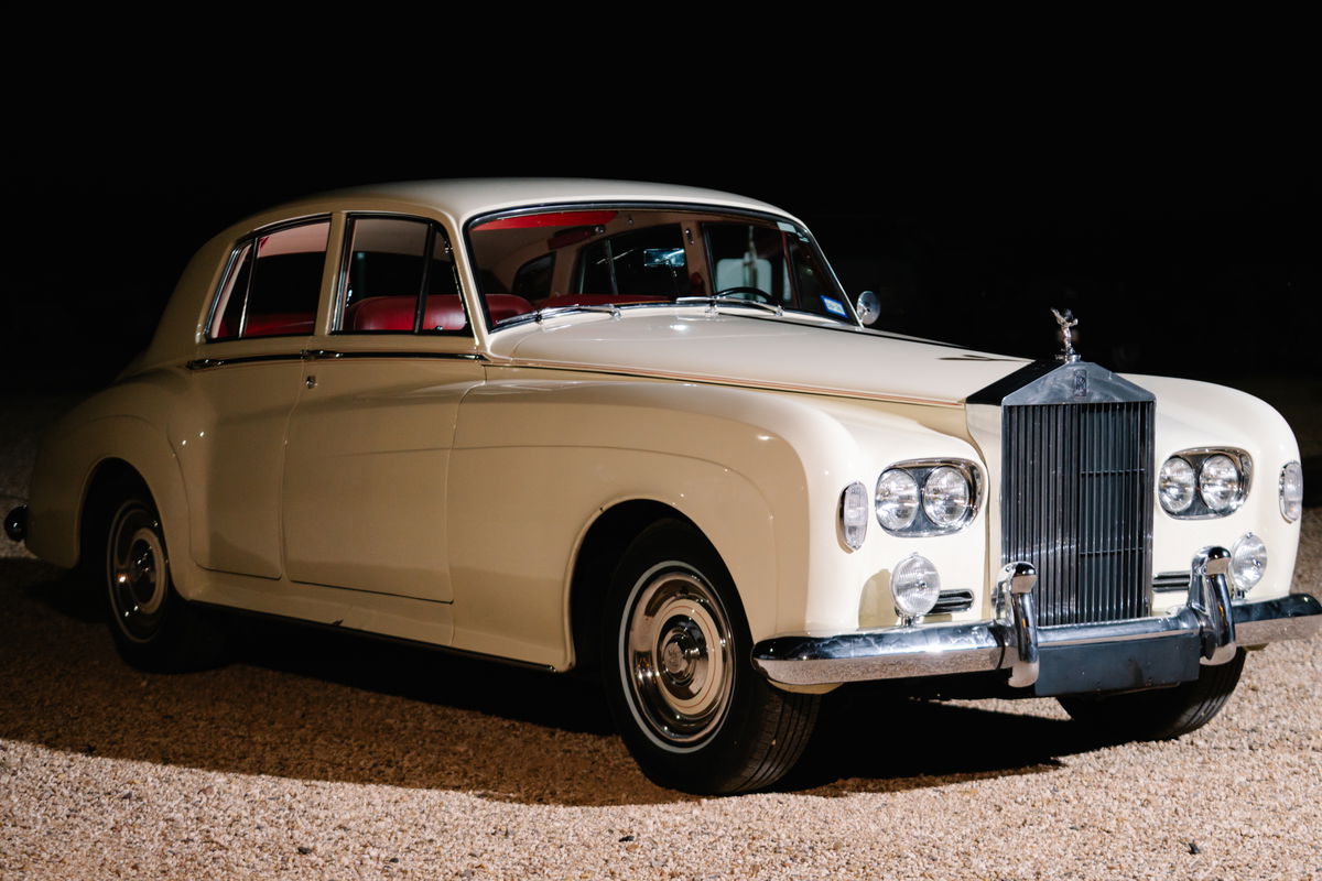 Vintage white 1963 Rolls Royce Silver Cloud parked outside a stone building storefront
