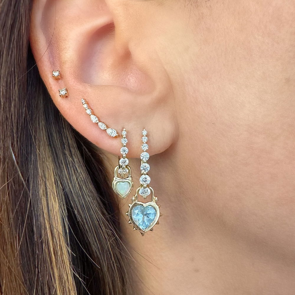 Vibrant heart shaped white opal bezel set in 14K yellow gold make the Single Beating Heart White Opal Charm sparkle. This tiny charm looks amazing on a Three Stories hoop earring or added to a detachable bale and hung on a Three Stories chain necklace or bracelet.Charms sold as singles. Hoop sold separately. Beating Heart White Opal Charm