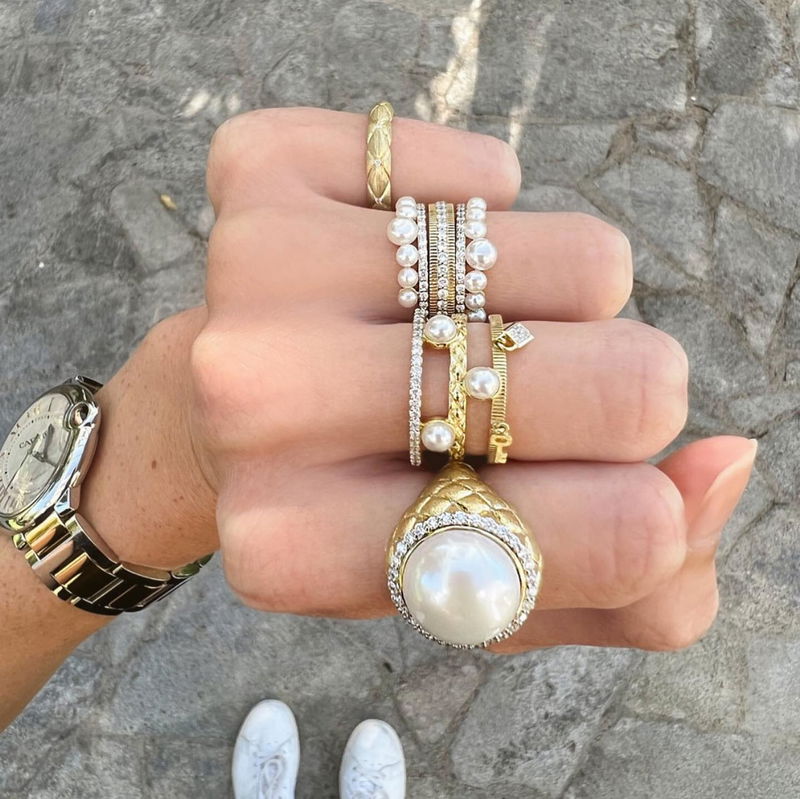 A hand stacked with gold and pearl rings