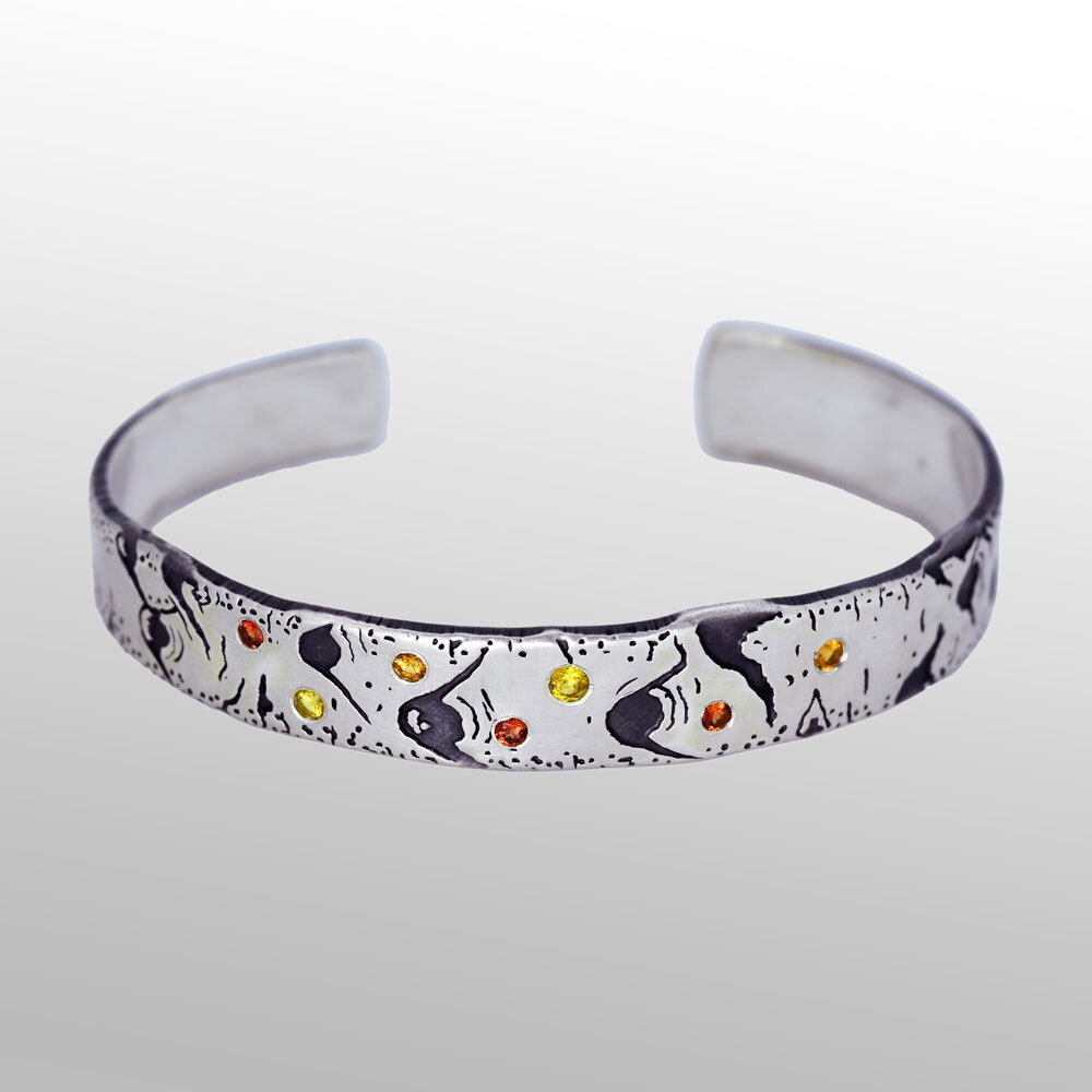 As if sprinkled by the morning dew, lovely gemstones adorn the bark of the Aspen tree. Hand-crafted by a talented jeweler, this cuff bracelet celebrates the love of nature while bringing joy to the wearer. Low tarnish formula Sterling silver, partially oxidized. 2.2mm and 2.5mm yellow sapphire, 2x 2mm Mandarin garnet, 3x 2mm red sapphire Aspen Allure Cuff Style Bracelet