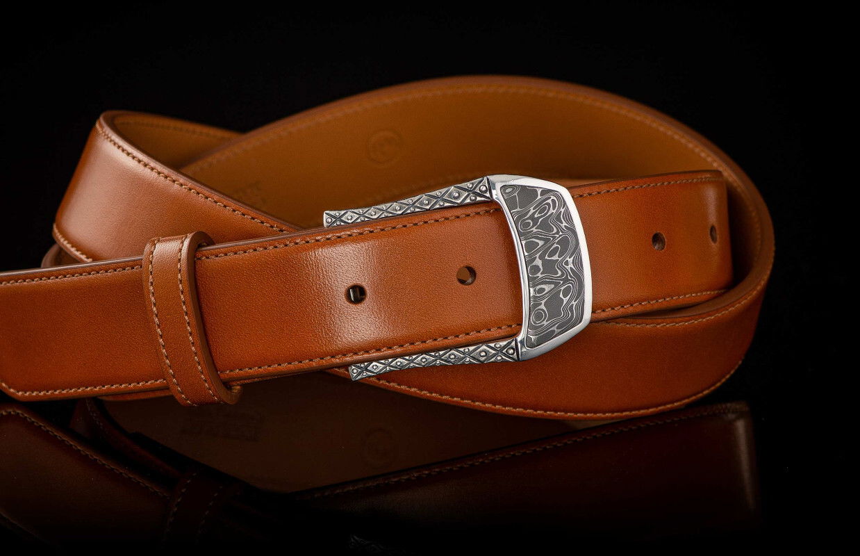 This beautiful belt buckle works from the street to the boardroom, and it creates an elegant accent to any attire. Sculpted in solid sterling silver, the highlight is a striking inlay of hand-forged stainless Damascus steel (our Intrepid pattern). 140 layers of three different alloys forged into one tapestry in steel, heat treated, etched and polished to reveal the unique pattern as the alloys dance together. Fits any 1.25” (1 and ¼” wide) belt that allows for interchanging buckles. BUCKLE 3 - DAMASCUS