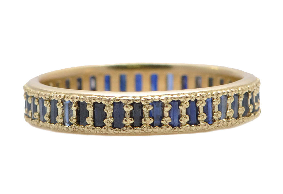 This 18K Yellow Gold Channel Set Blue Sapphire Baguette Stack Band Ring is a dazzling accessory for any occasion. Expertly crafted and featuring a channel of sparkling blue sapphire baguettes, this luxurious two-tone ring is the perfect addition to your jewelry collection. The 18K yellow gold and vivid blue sapphire gemstones create a powerful contrast that adds a sophisticated touch to any ensemble. Wear this stunning piece to dress up any casual outfit or to complete a chic evening look. This ring is sure to become a treasured favorite. Baguette Stack Band Ring