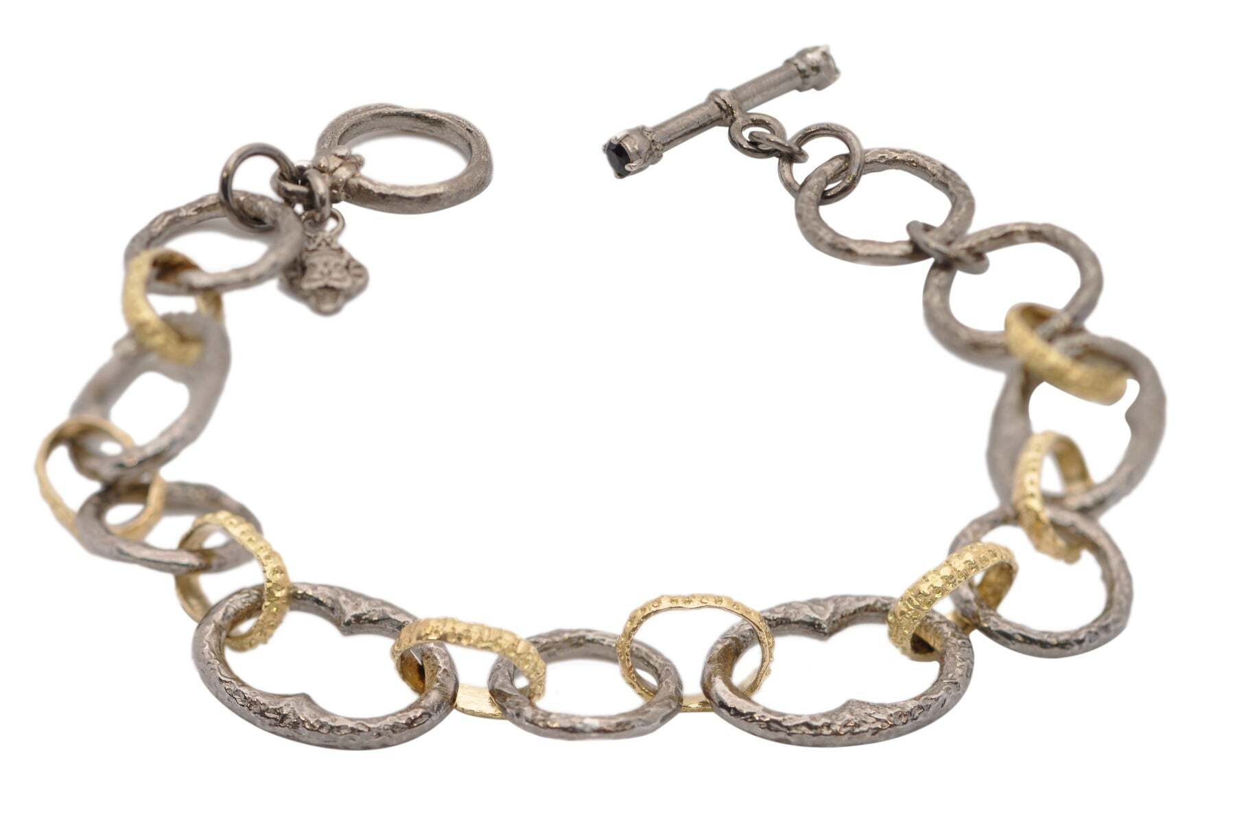 This stunning bracelet is sure to become one of your favorite pieces! Crafted from 18k yellow gold and grey rhodium finished sterling silver, this 8" textured chain link bracelet sparkles with alternating gold and grey silver links. Its toggle closure is encrusted with black sapphires, adding a unique touch to a classic design. This is an elegant addition to any jewelry collection! ALTERNATING TEXTURED CHAIN LINK BRACELET