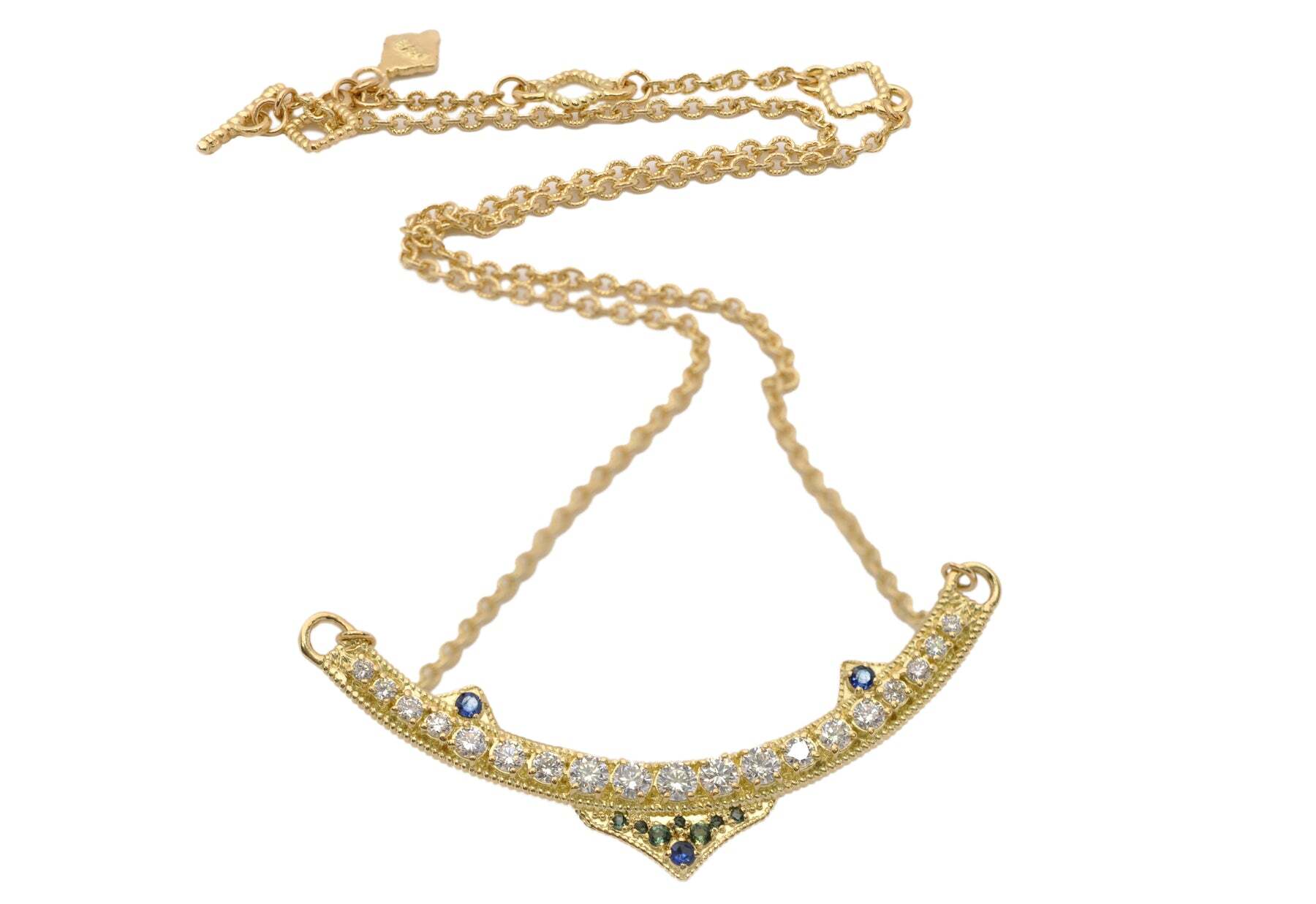 This 18K yellow gold statement necklace is a timeless and refined piece of jewelry boasting a unique curved bar design. Adorned with blue-green tourmalines, blue sapphires, and 1.10 total carat weight of white brilliant diamonds, this necklace radiates with a brilliant sparkle. With a toggle closure, this necklace is adjustable at 15.5 inches, 16.5 inches, and 17.5 inches, making it the perfect accessory for any neckline. Showcase your unique style with this elegant yet modern statement necklace. 17.5" STATEMENT NECKLACE WITH YELLOW GOLD CURVED BAR