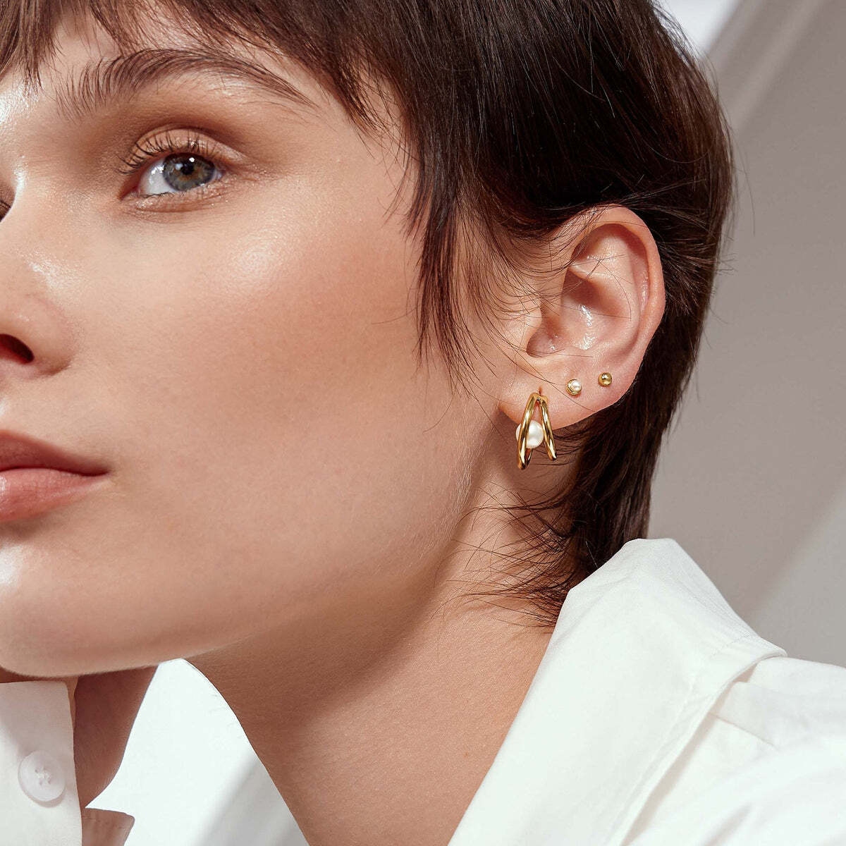 Product Description: With double loop design teamed with a pearl, these dainty huggies bring out unique look for you. Simply style with your favourite studs, hoops and ear cuffs for elevating your elegance and confidence. Product Details: • Material: 925 Sterling Silver with 14kt Gold Plating with Pearl• Size: 17.5 x Gold Duo Freshwater Pearl Stud Hoops– Ania Haie US